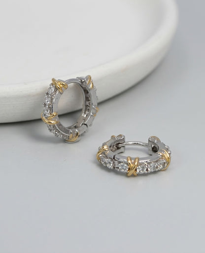 Two-tone CZ huggie hoop earrings with gold criss-cross X detail on white marble surface 