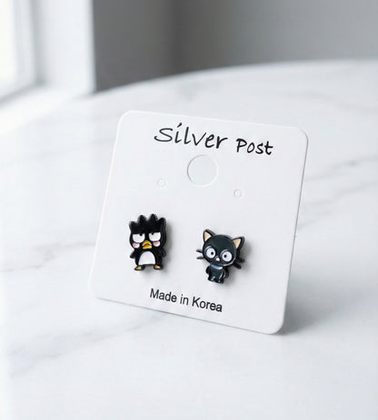 Close up of Badtz-Maru penguin and Chococat black cat stud earrings on white display card with silver post label, handmade in Korea