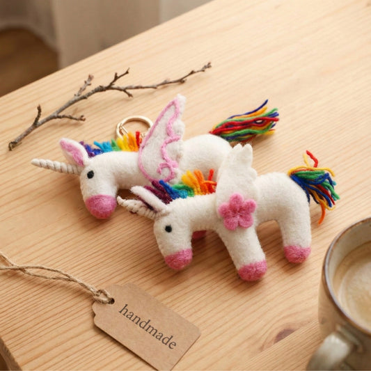 Handmade needle felted rainbow unicorn keychain with pink stitch wings and 3D flower wings on wooden table with handmade tag