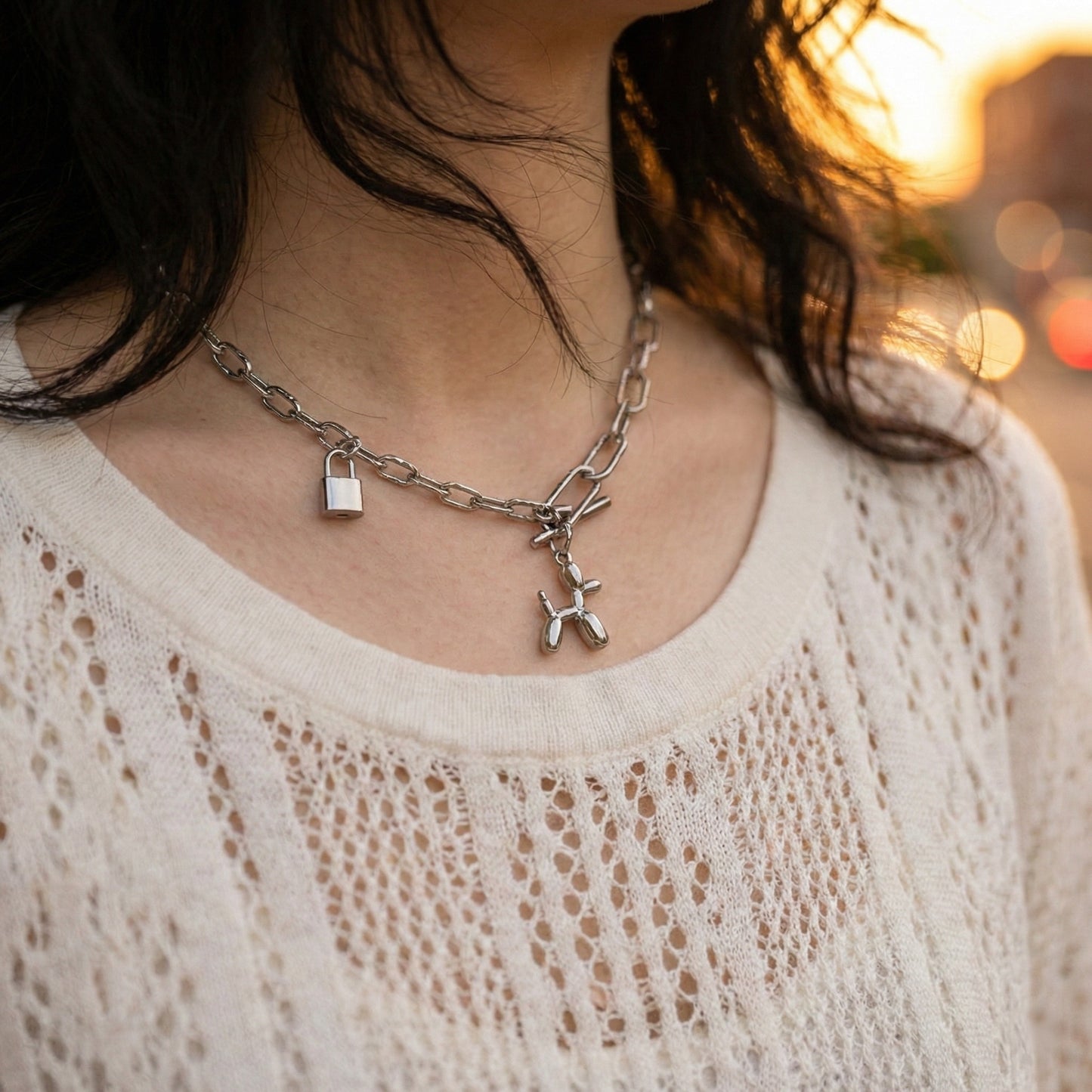 Close-up of woman wearing asymmetrical chain necklace with balloon dog charm and padlock pendant