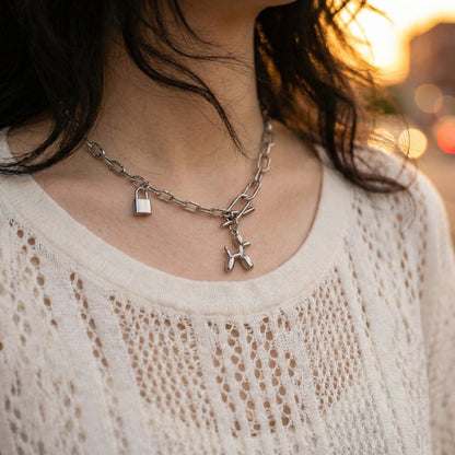 Close-up of woman wearing asymmetrical chain necklace with balloon dog charm and padlock pendant