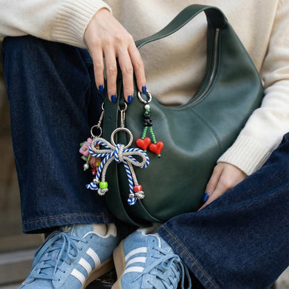 Woman holding forest green hobo bag with blue and yellow striped rhinestone rope bow bag charm with heart charms