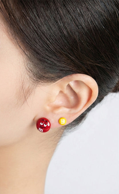 Woman wearing red and yellow M&M's character earrings on white background, side profile close-up showing double piercing style with playful candy-inspired studs, 925 sterling silver posts, handmade in South Korea by 8ttitto8