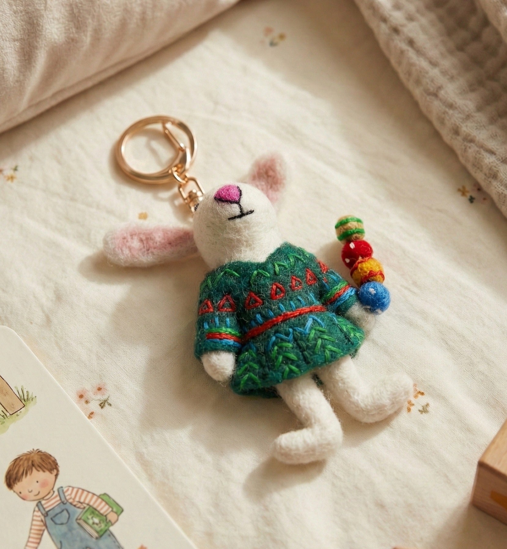 Handmade wool felt rabbit keychain with green sweater holding colorful candied fruit on gold ring