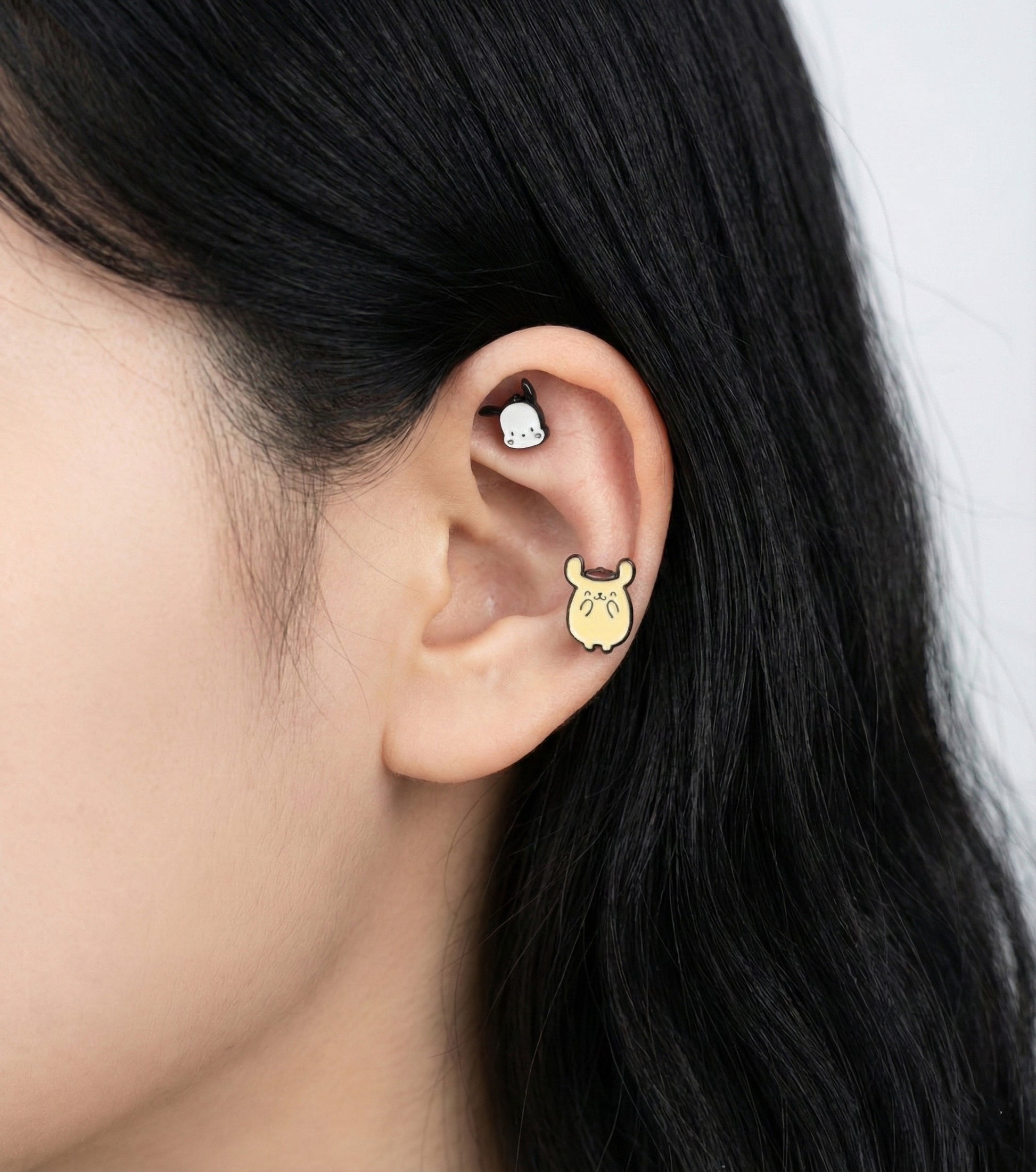 Model wearing Pompompurin titanium piercing on ear with Kuromi character showing mix and match style