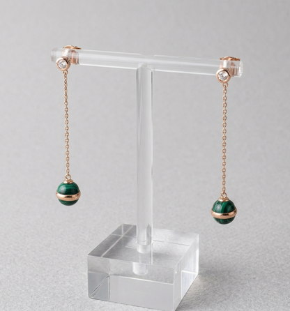 Natural malachite ball drop earrings displayed on acrylic T-bar stand, showing rose gold chain, CZ bezel stud top, and 8mm green malachite sphere with saturn-ring band detail