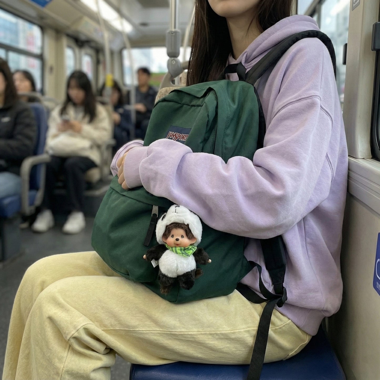 Kawaii panda Monchhichi keychain attached to green JanSport backpack on subway