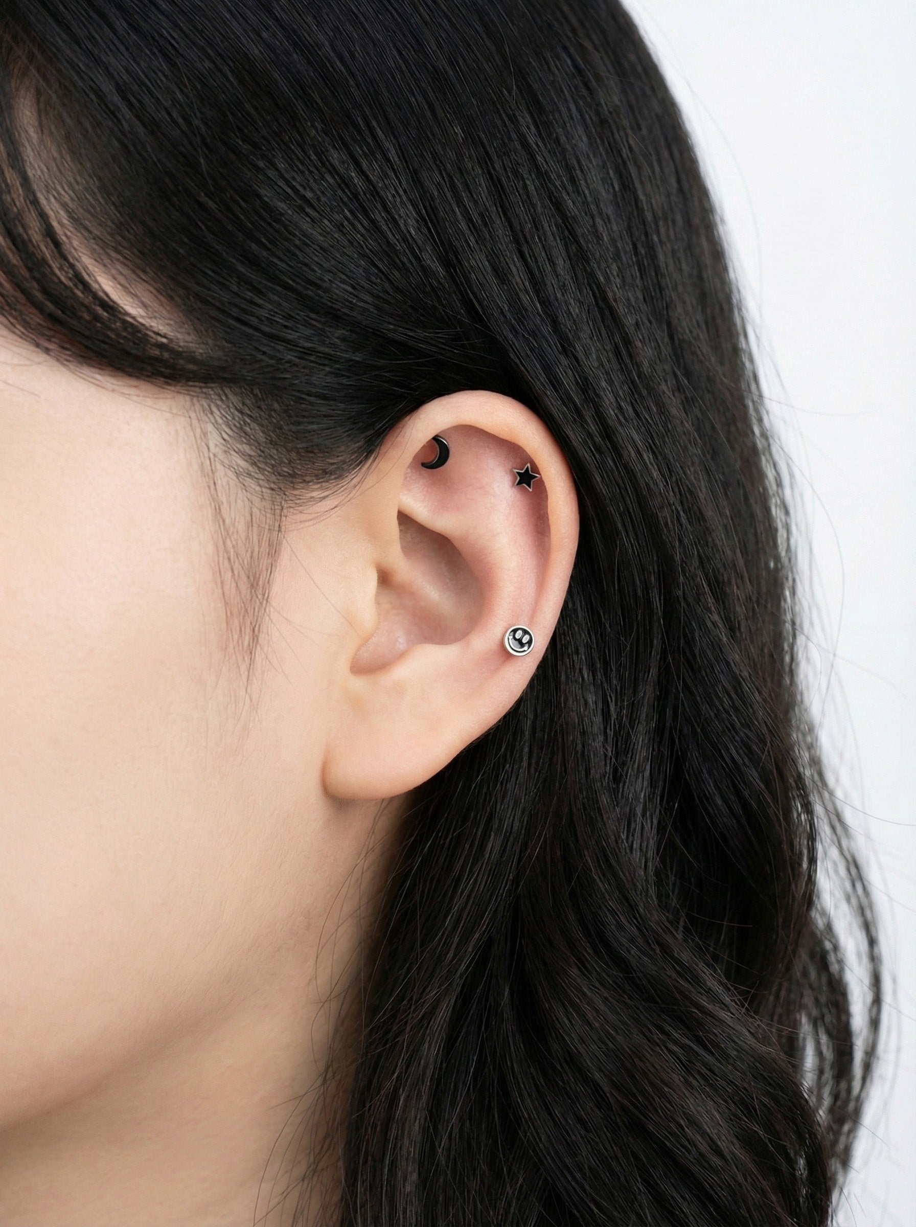 Woman wearing celestial cartilage piercings - star on helix, moon on tragus, smiley on lobe