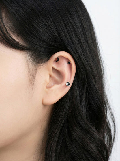 Woman wearing celestial cartilage piercings - star on helix, moon on tragus, smiley on lobe