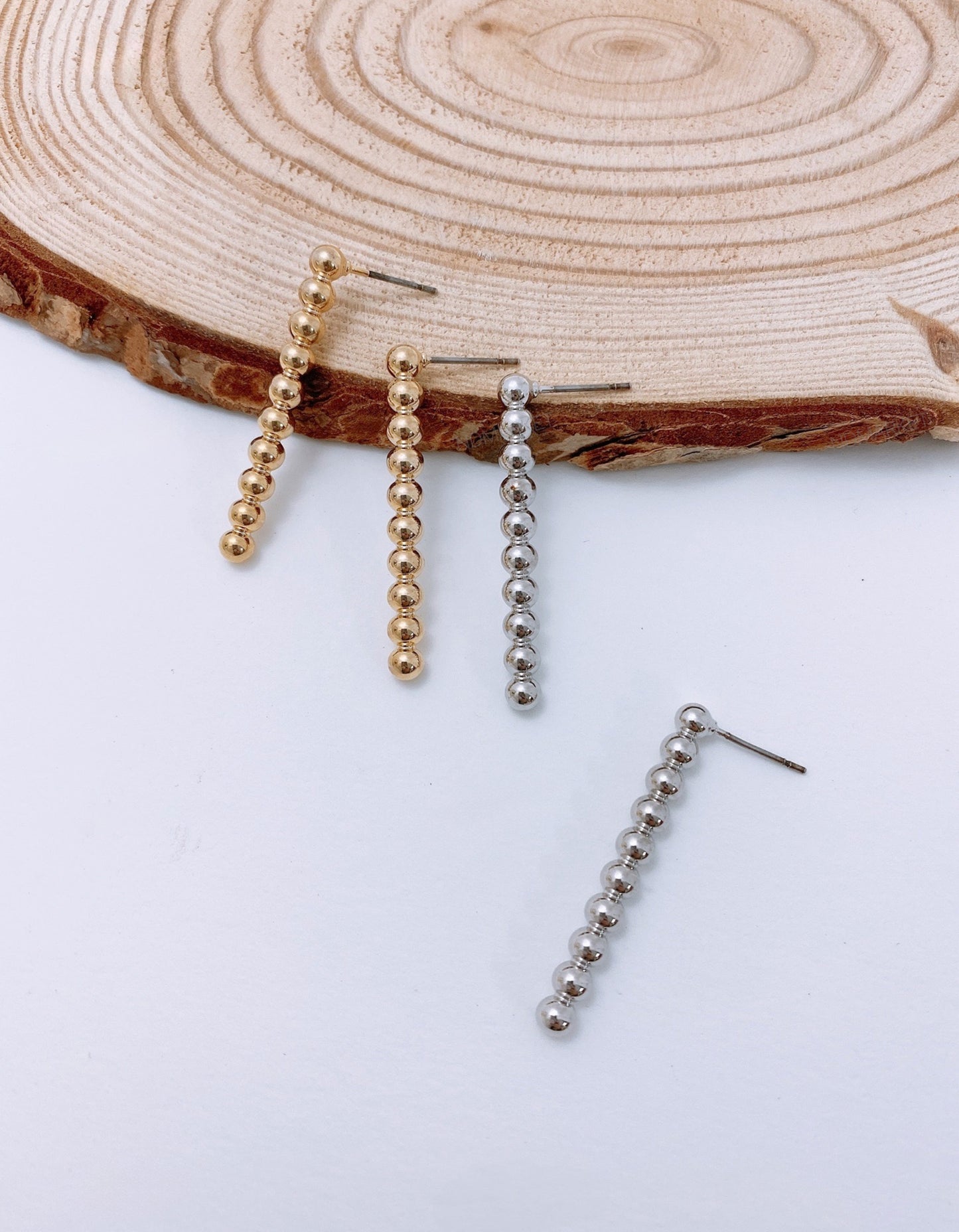 Gold and silver fixed ball bar drop earrings on natural wood background