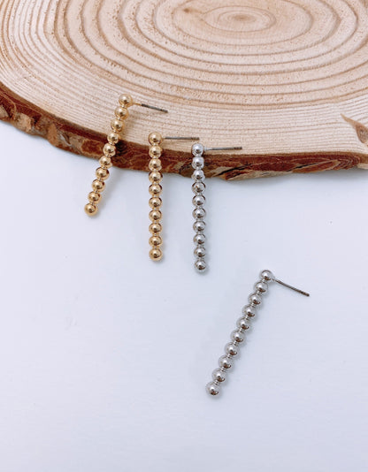 Gold and silver fixed ball bar drop earrings on natural wood background