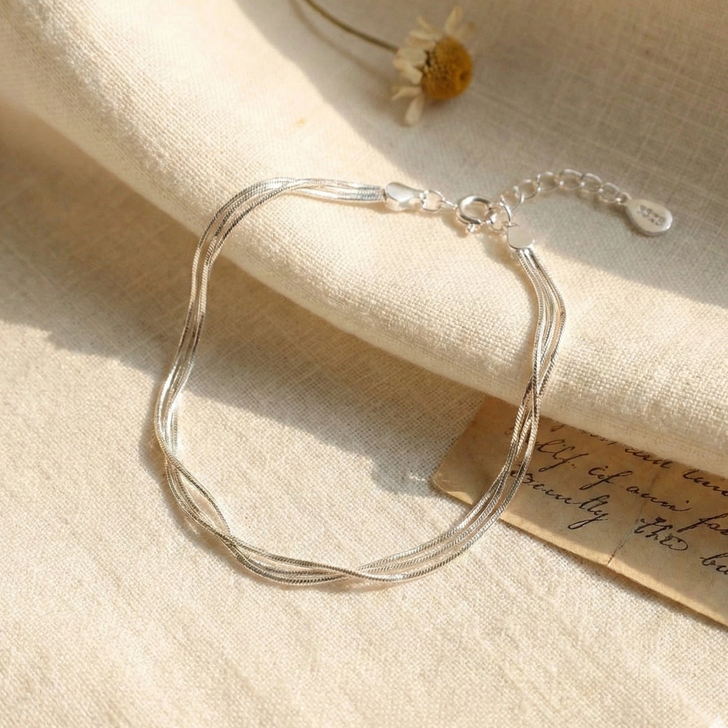 925 sterling silver layered snake chain bracelet flat lay with daisy flower and vintage letter