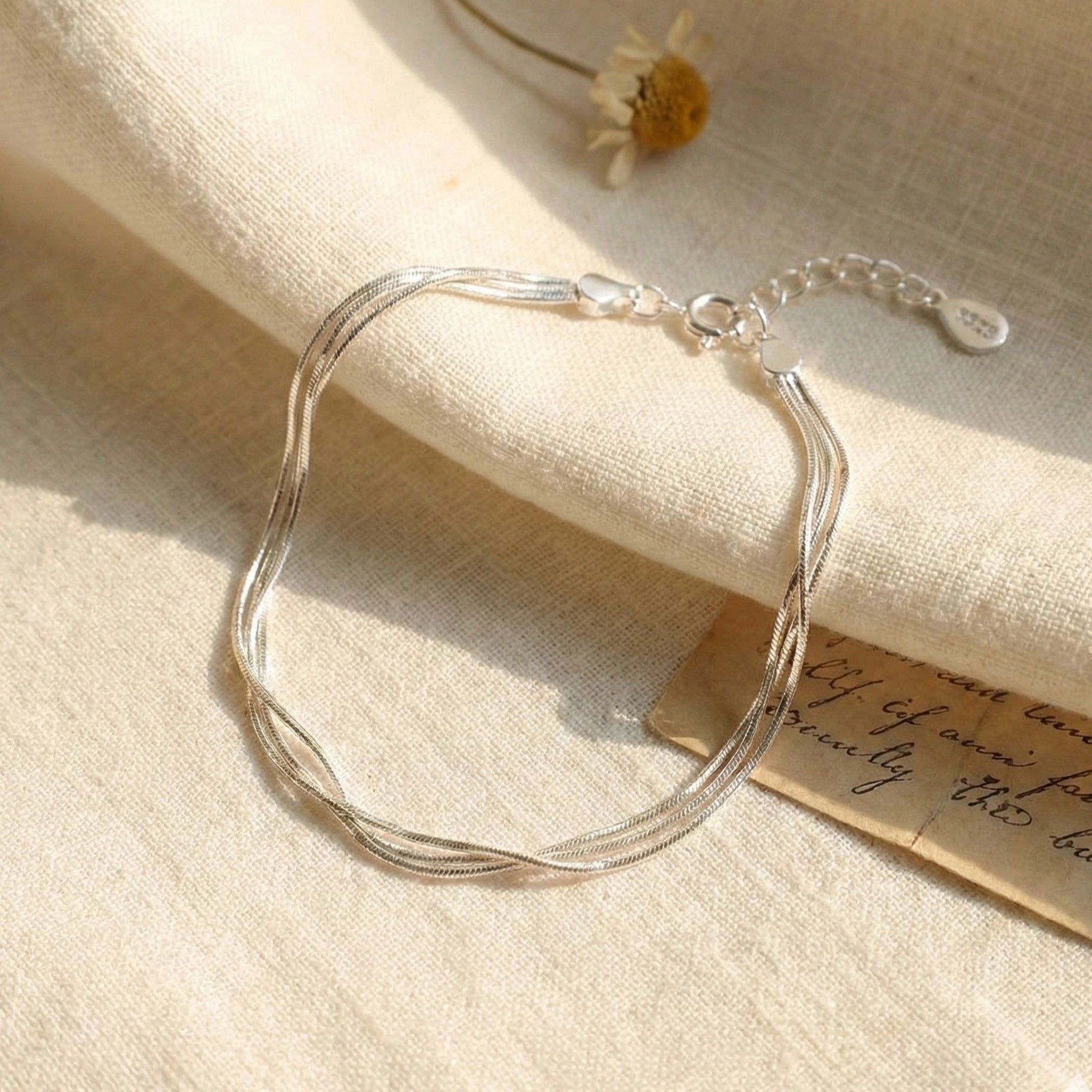 925 sterling silver layered snake chain bracelet flat lay with daisy flower and vintage letter