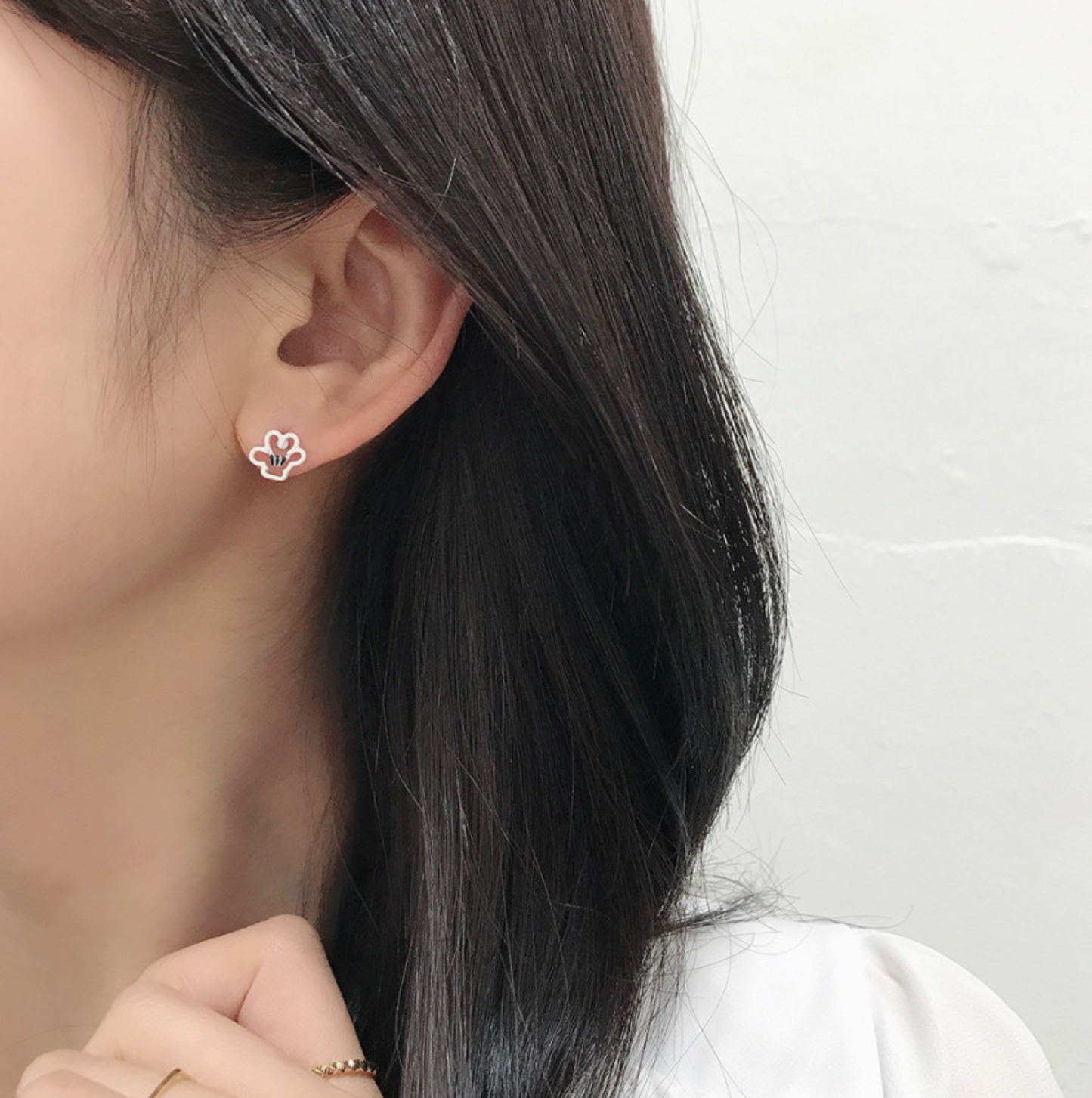 Close-up of ear wearing a white Mickey glove earring, styled with long black hair and a minimal look.
