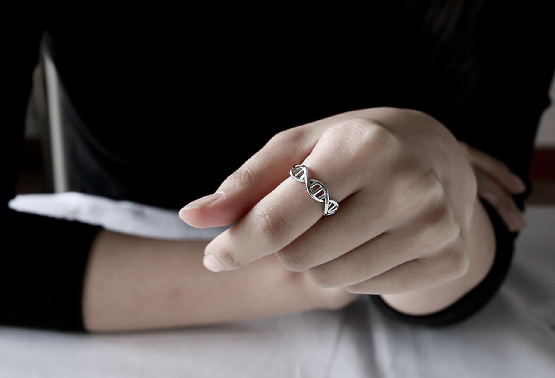 Model wearing a sterling silver DNA double-helix ring on the index finger, minimal black outfit.