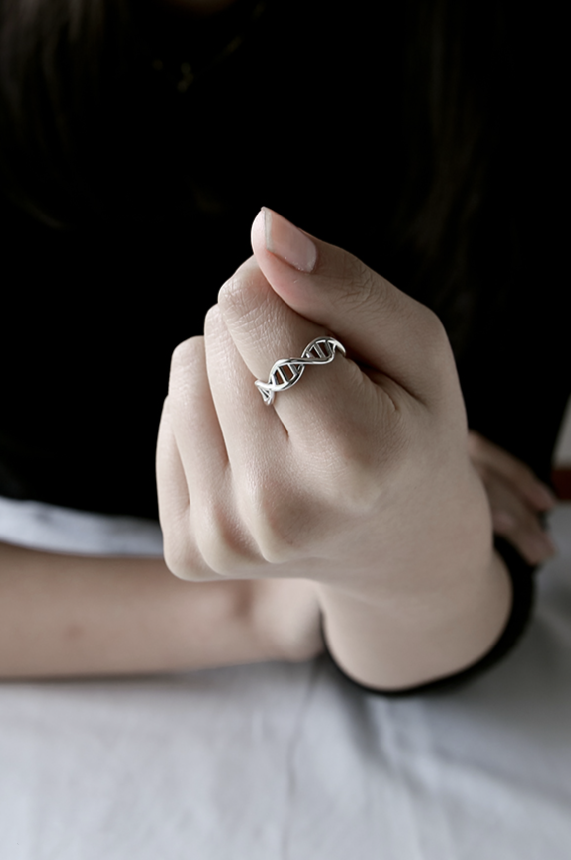 Close-up of a hand showing a sterling silver DNA helix ring, soft natural lighting.