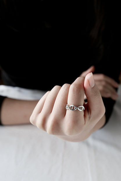 Model’s hand holding a sterling silver DNA helix ring, artistic lifestyle shot.