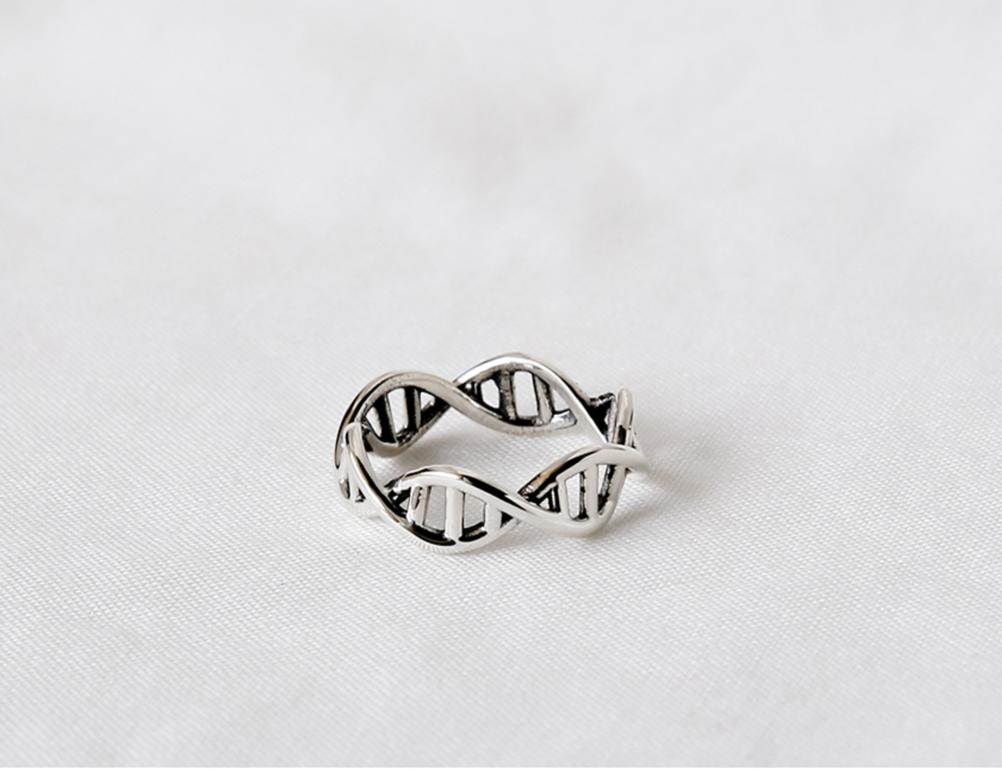 Sterling silver DNA open band ring resting on a soft white fabric background.