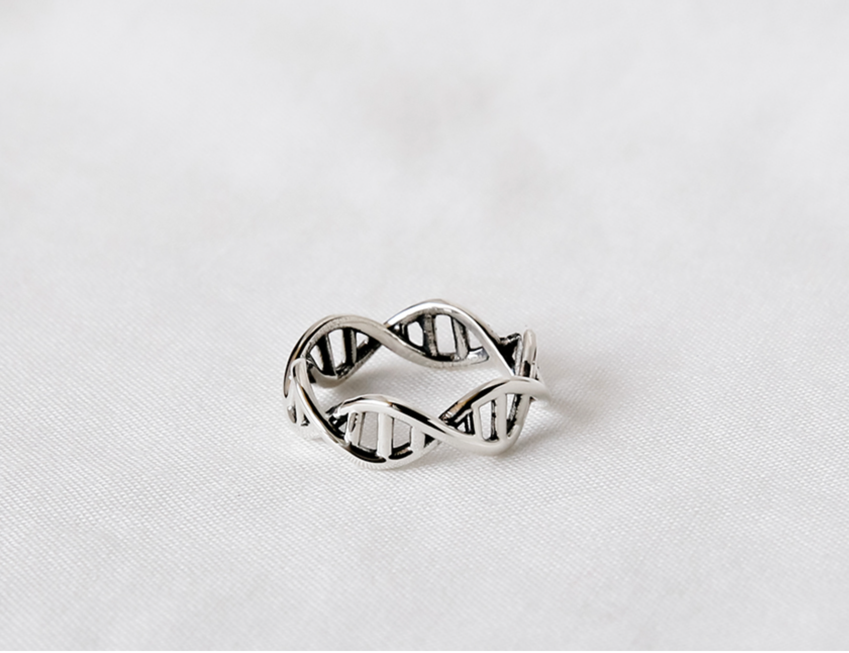 Sterling silver DNA open band ring resting on a soft white fabric background.