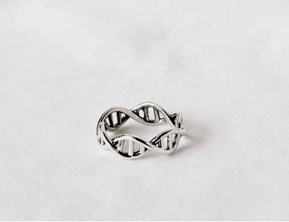 Sterling silver DNA open band ring resting on a soft white fabric background.