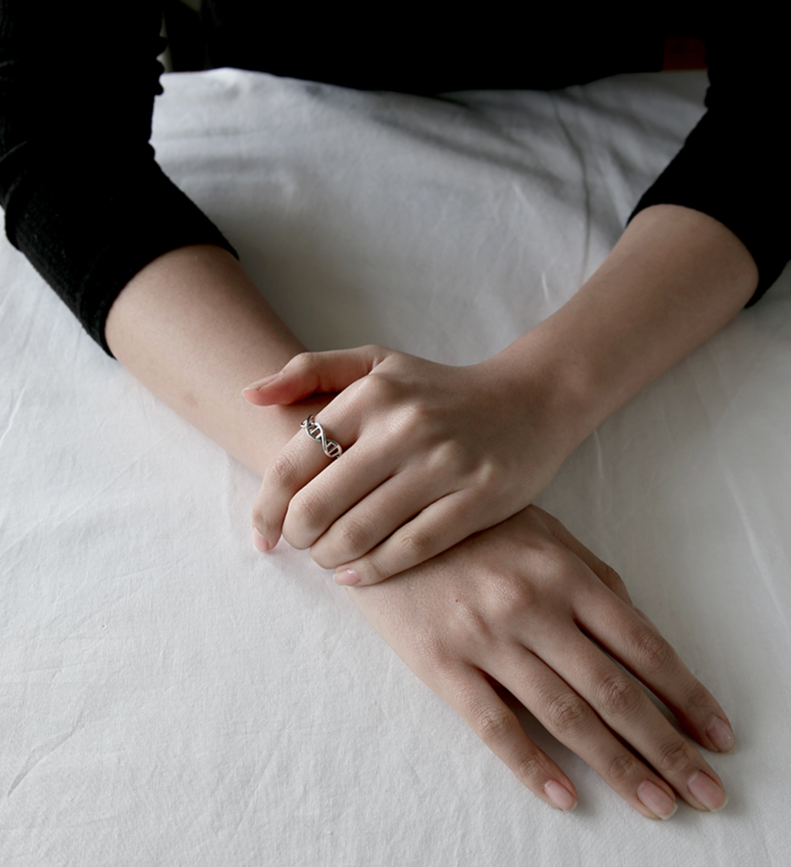 Two hands resting together while wearing a sterling silver DNA double-helix ring