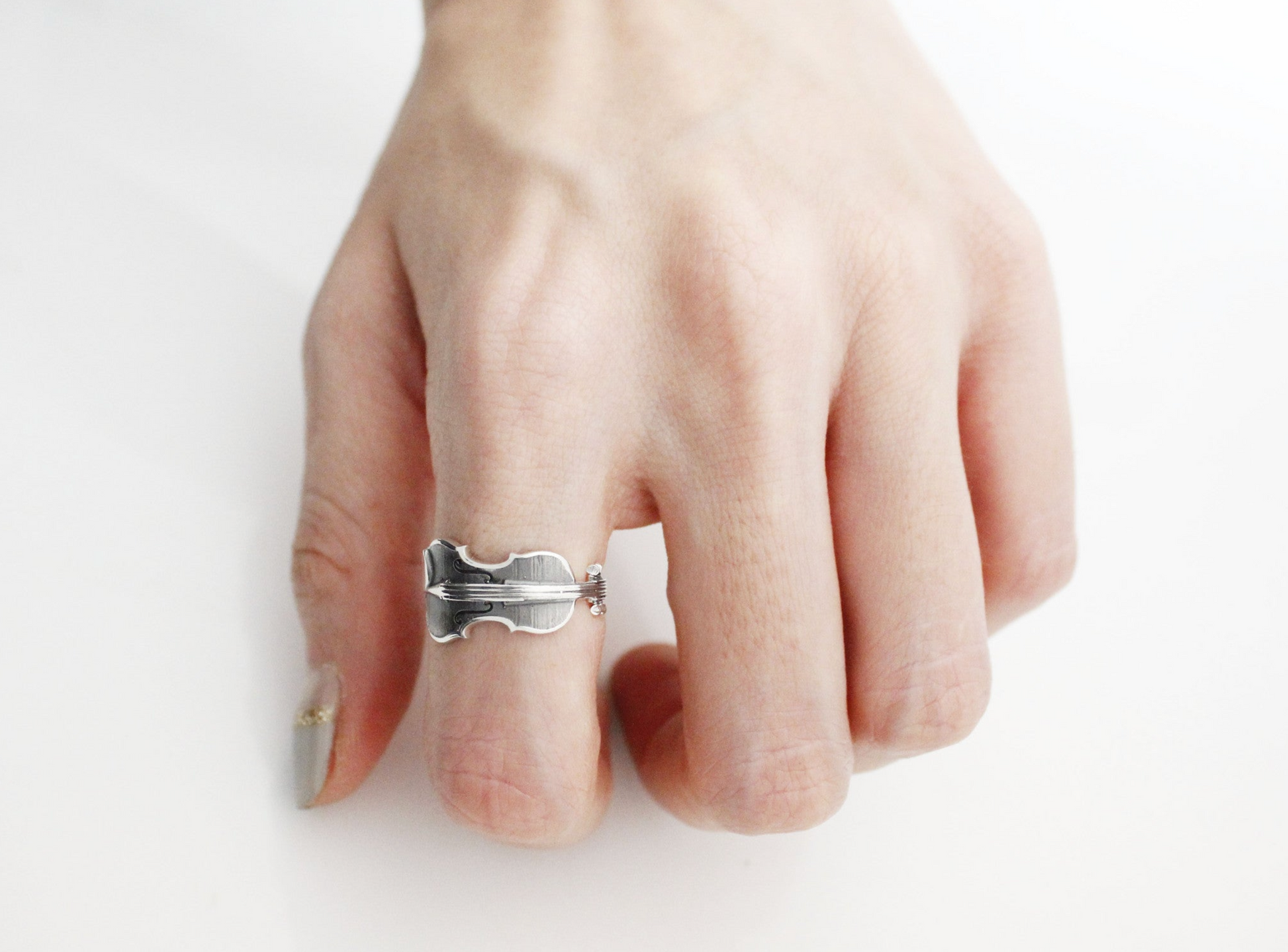 Instrument-shaped silver ring with detailed carving worn on middle finger