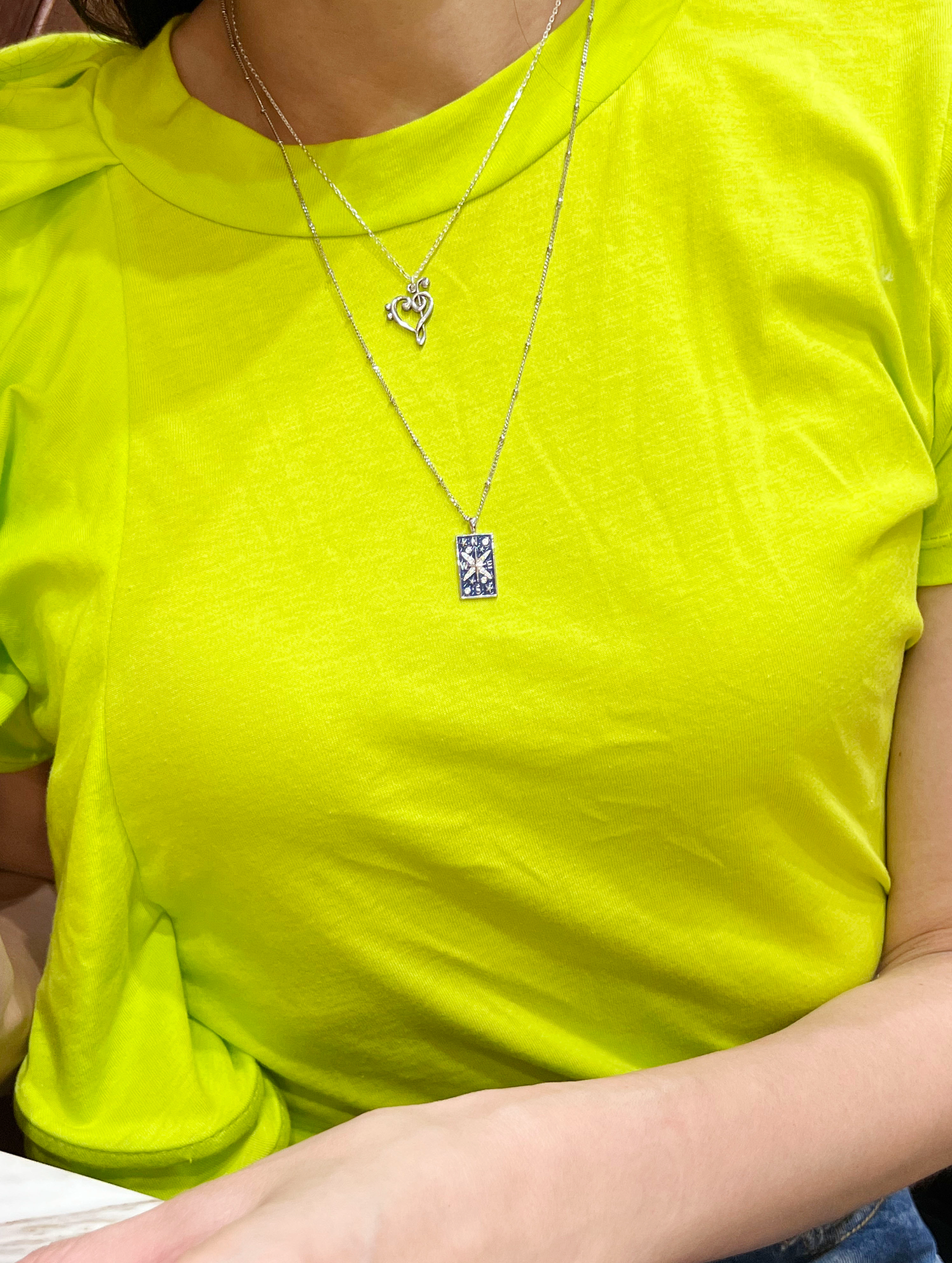 Music note necklace layered with other necklaces on model
