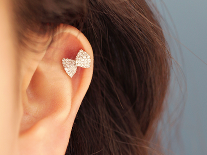 Silver bow barbell earring styled on the inner ear cartilage, sparkling under soft natural light.