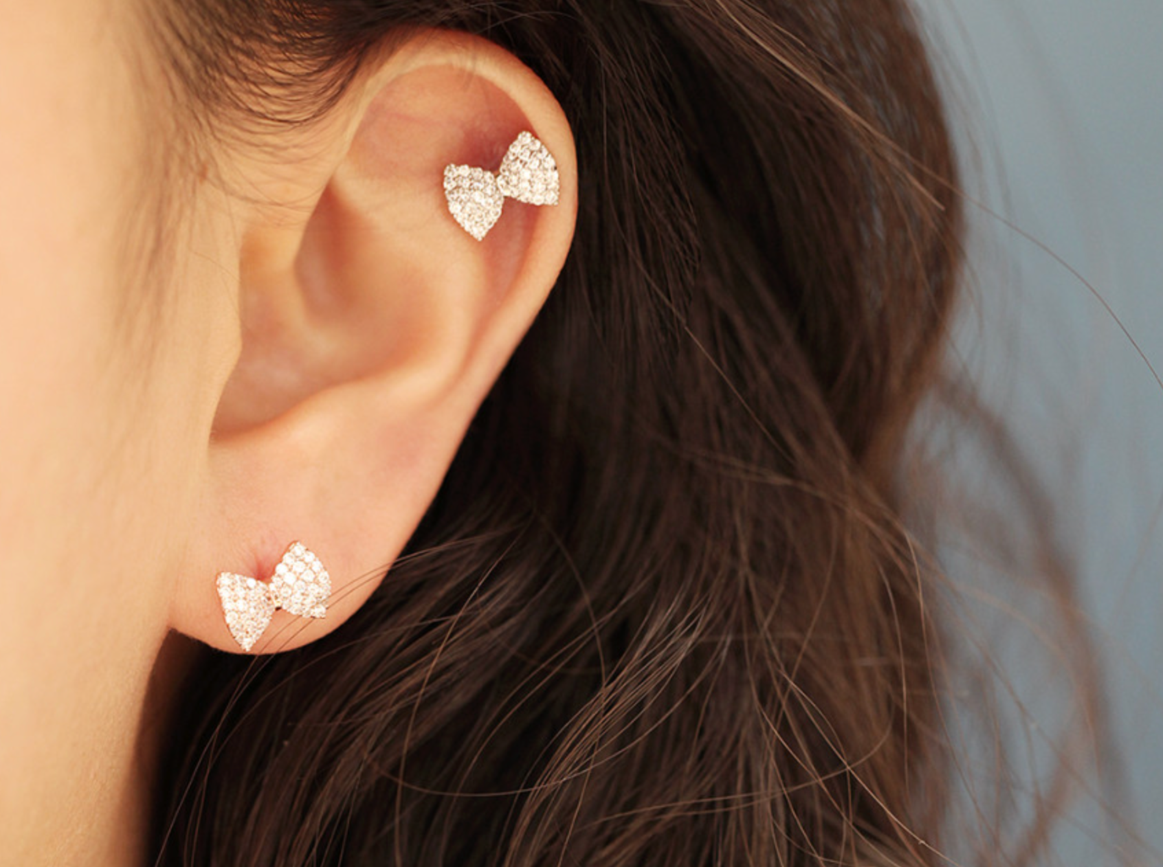 Two silver bow earrings layered on one ear—one on the helix and one on the lobe—styled in a chic, balanced look