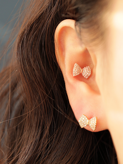 Rose gold bow barbell earrings styled on both lobe and upper cartilage, catching warm light against dark hair