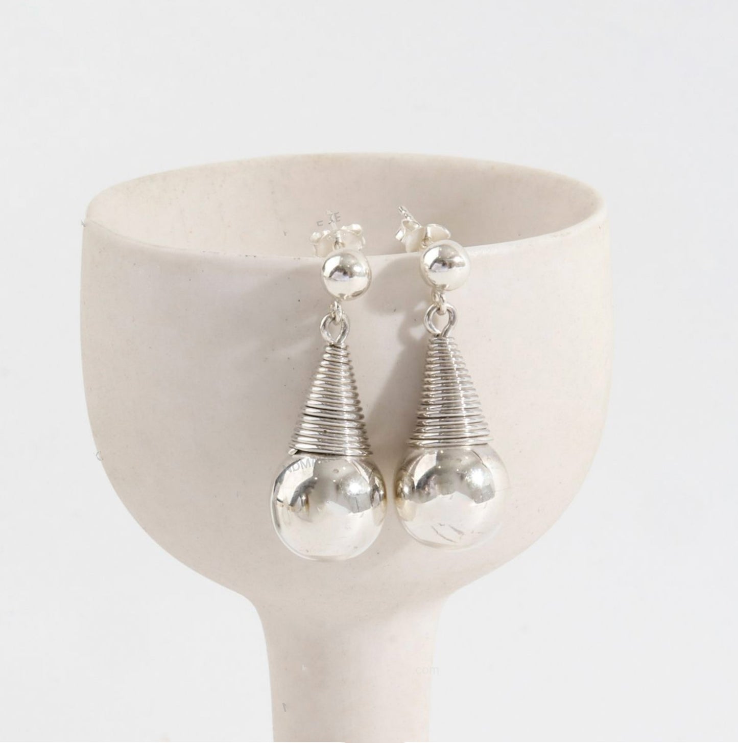 Close-up detail of sculptural wire-wrapped coil and polished silver sphere earrings