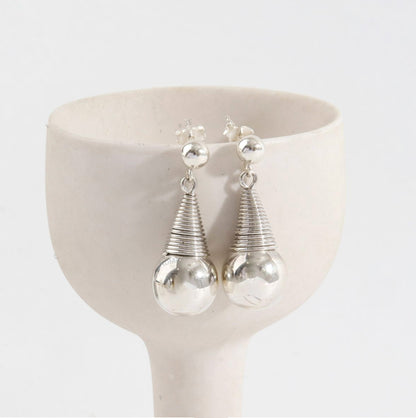 Close-up detail of sculptural wire-wrapped coil and polished silver sphere earrings