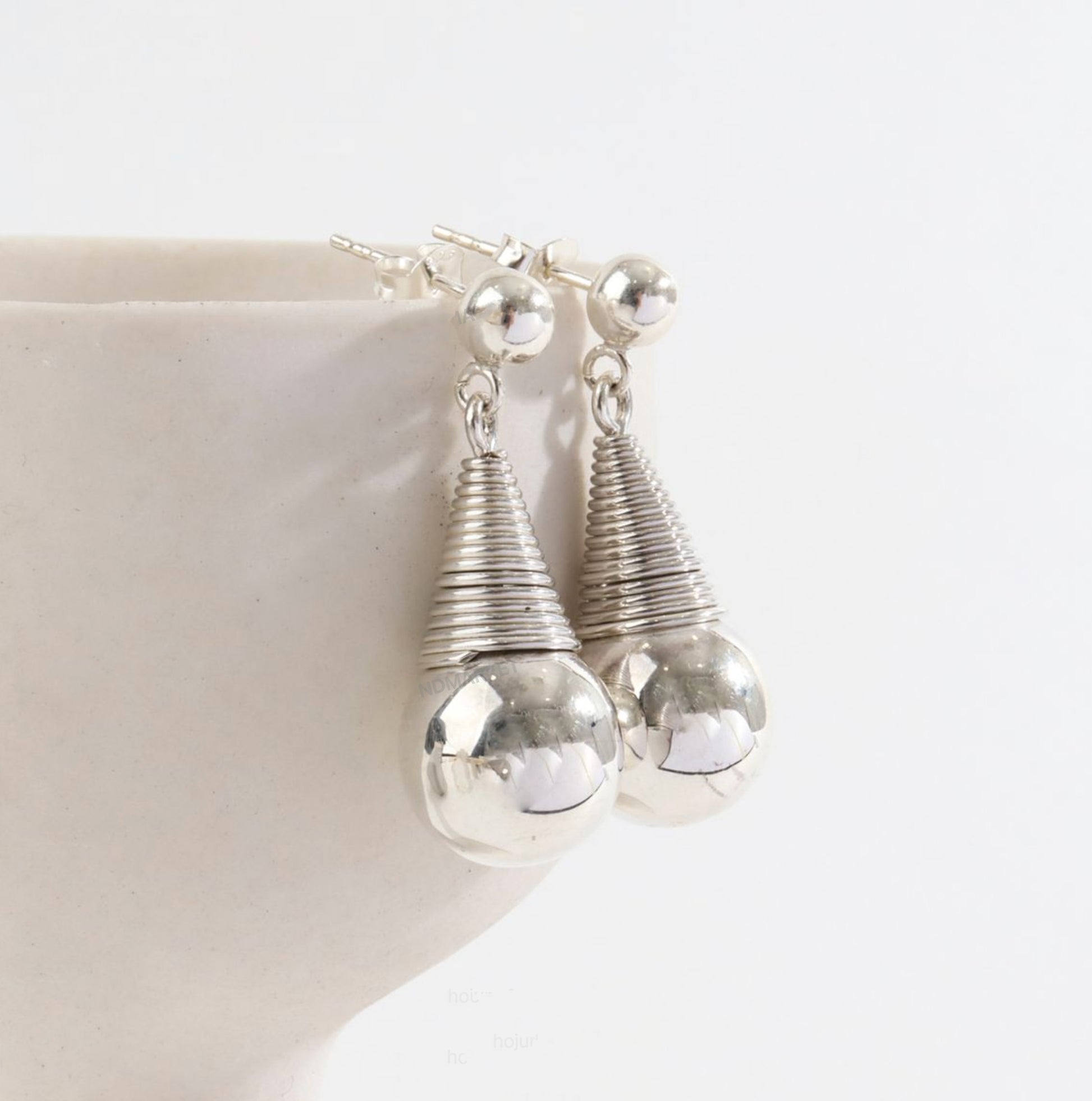 Close-up detail of sculptural wire-wrapped coil and polished silver sphere earrings