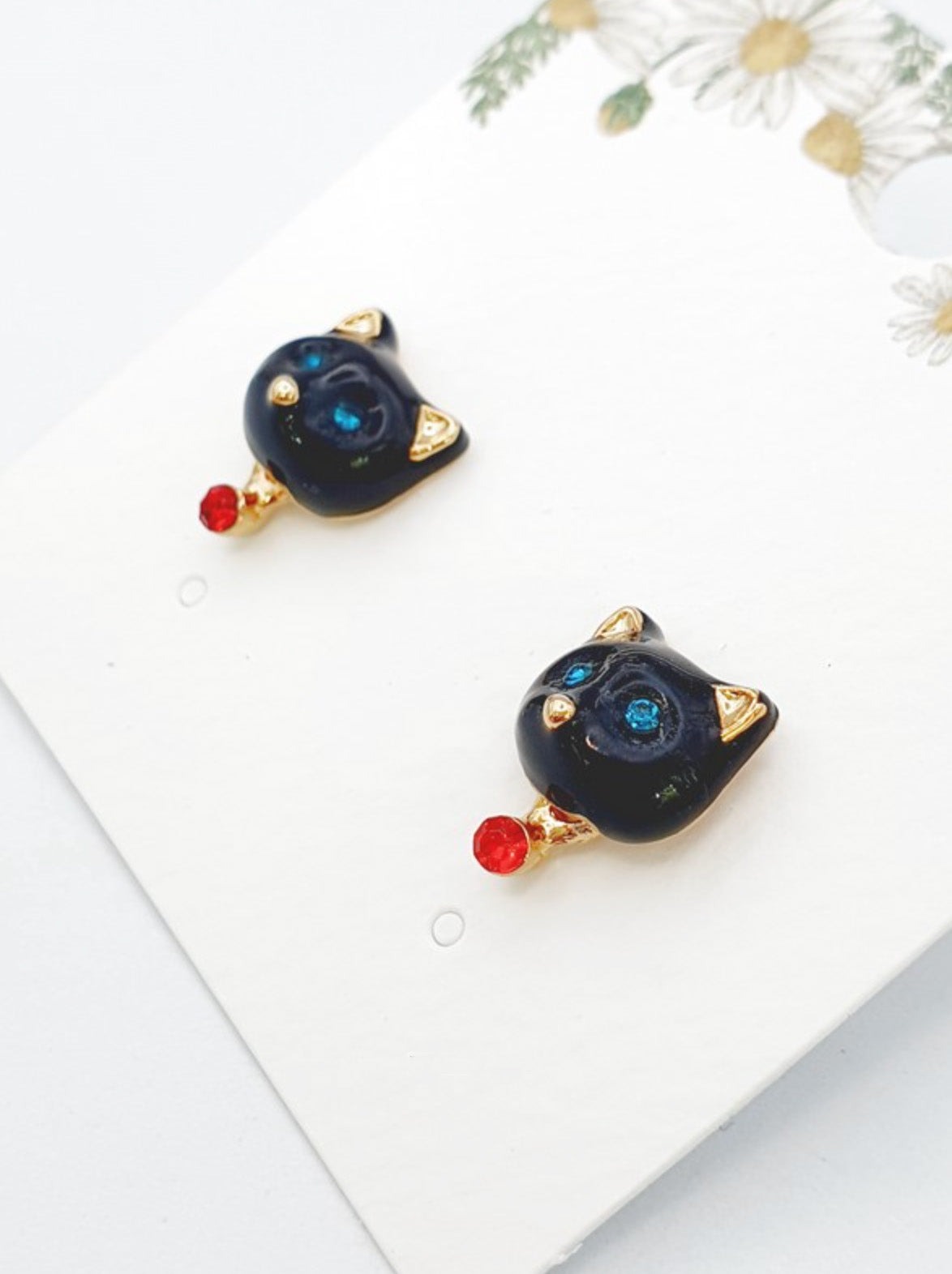 Black enamel cat-shaped stud earrings with blue crystal eyes, gold ear tips, and a small red crystal drop accent