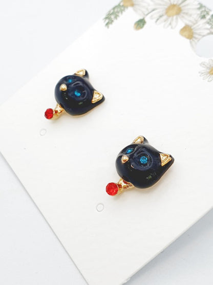 Black enamel cat-shaped stud earrings with blue crystal eyes, gold ear tips, and a small red crystal drop accent