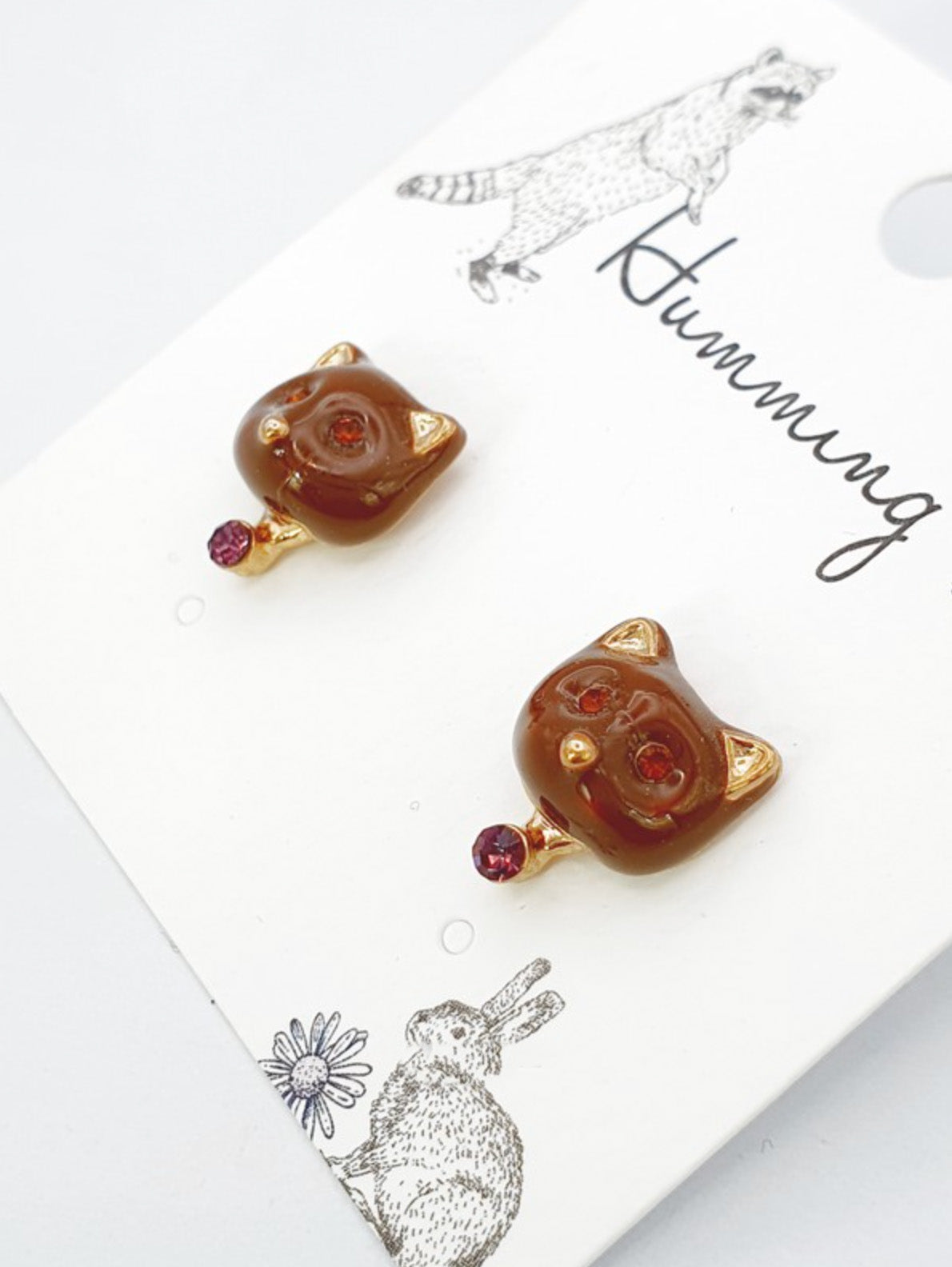 Brown enamel cat-shaped stud earrings with amber crystal eyes, gold ear tips, and a small purple crystal drop