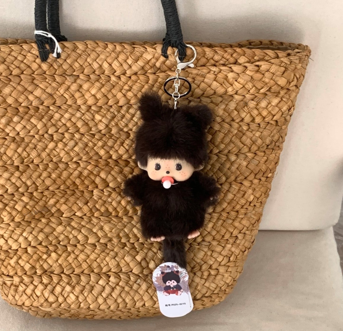 Furry black plush doll with pacifier clipped to a woven straw bag, styled as a keychain charm.