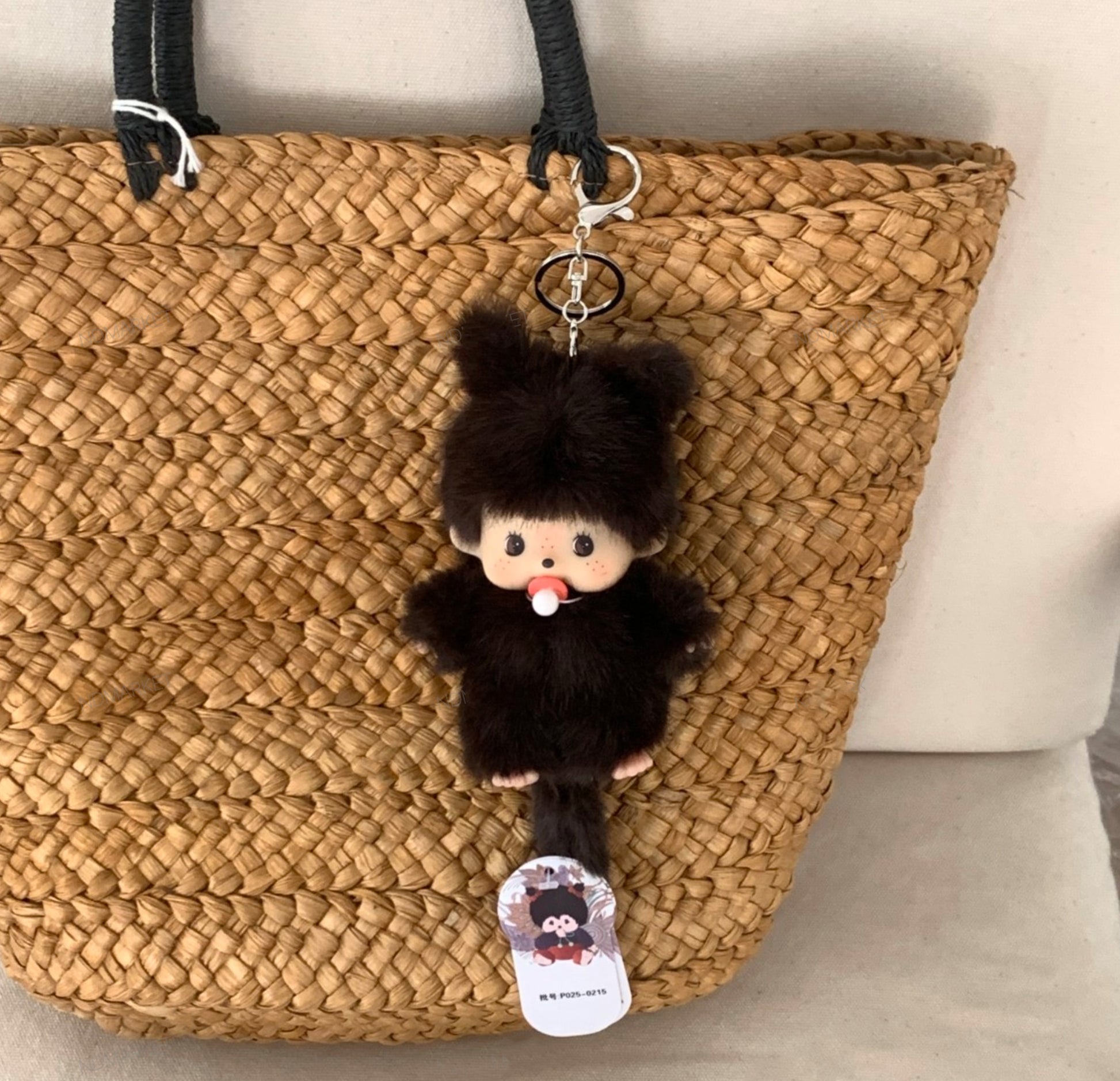Furry black plush doll with pacifier clipped to a woven straw bag, styled as a keychain charm.