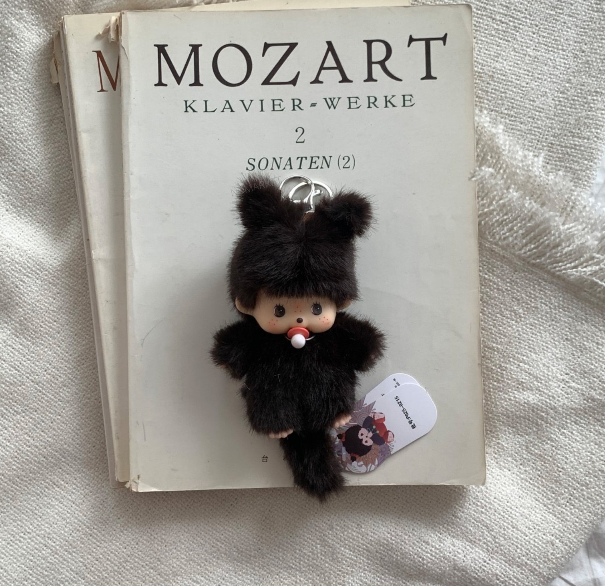 Dark brown plush doll with pacifier keychain displayed on a Mozart sonata sheet music book.