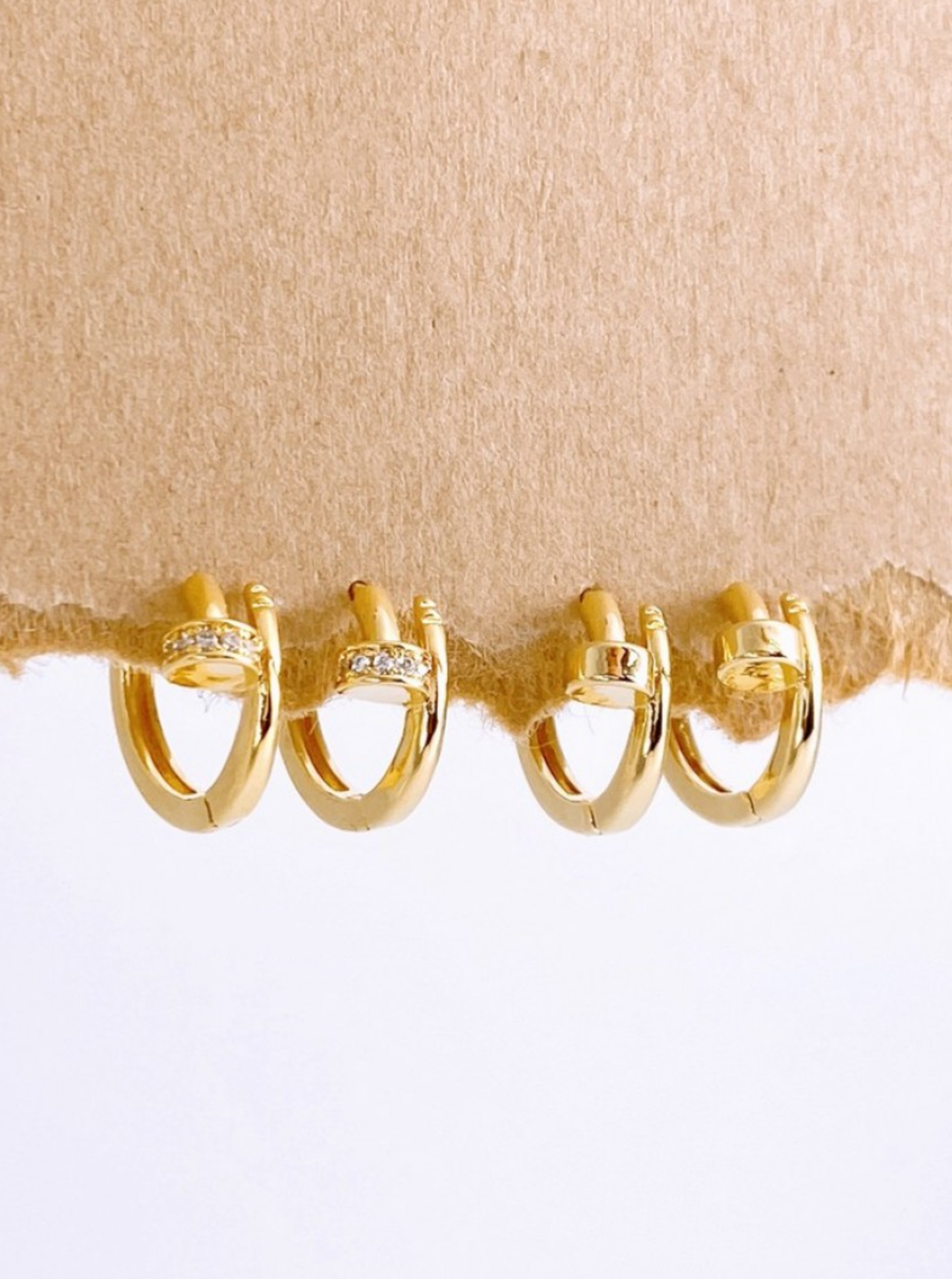 Set of gold hoop earrings displayed on textured brown paper, showcasing cubic and plain variants.