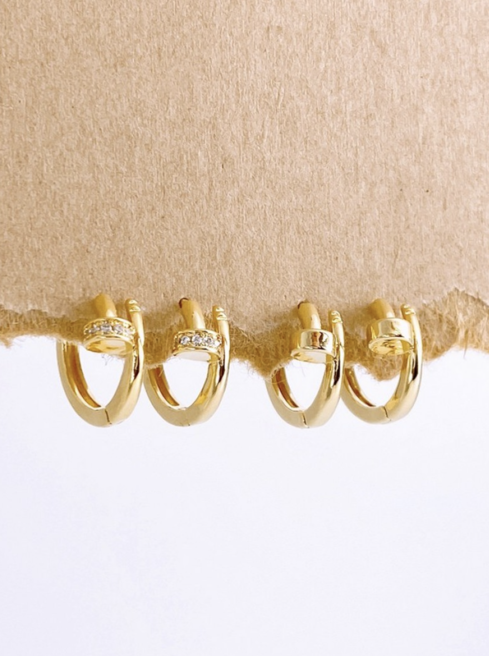 Set of gold hoop earrings displayed on textured brown paper, showcasing cubic and plain variants.