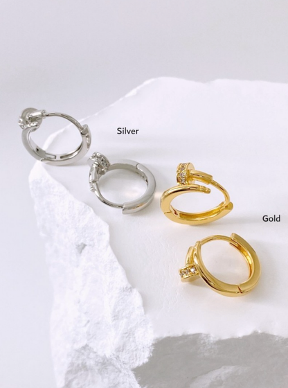 Product flat lay of gold and silver hoop earrings on white stone background, labeled by color.
