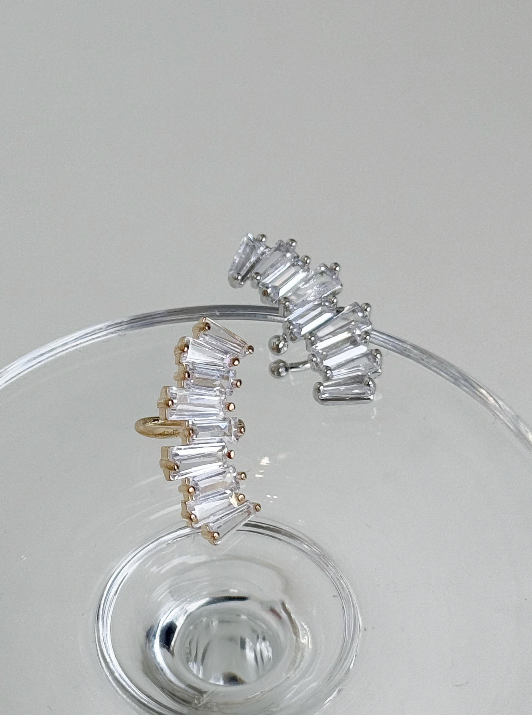 Gold and silver baguette-cut cubic zirconia ear cuffs displayed on a clear glass surface, brass material, handmade in Korea.
