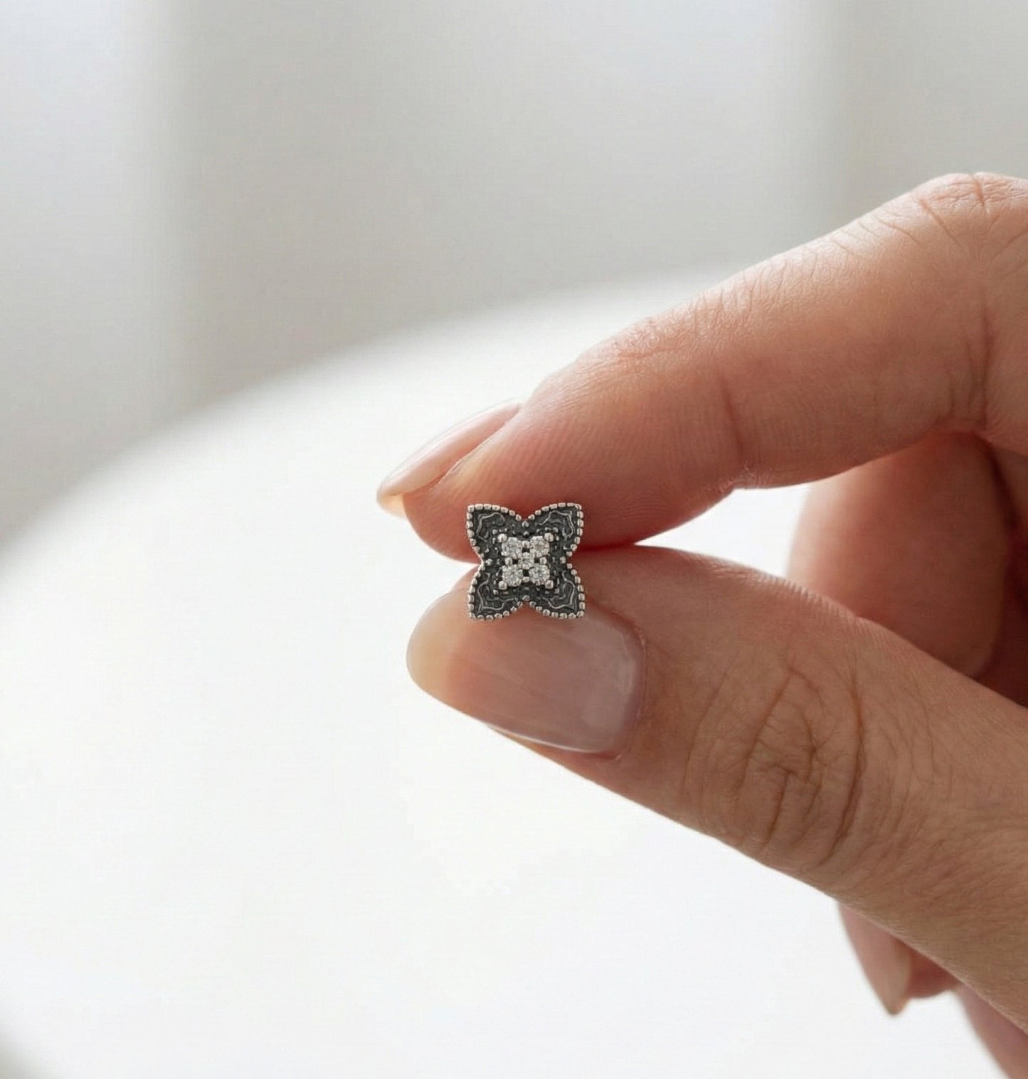 Quatrefoil flower cartilage stud with milgrain edging and crystal accents held between fingers