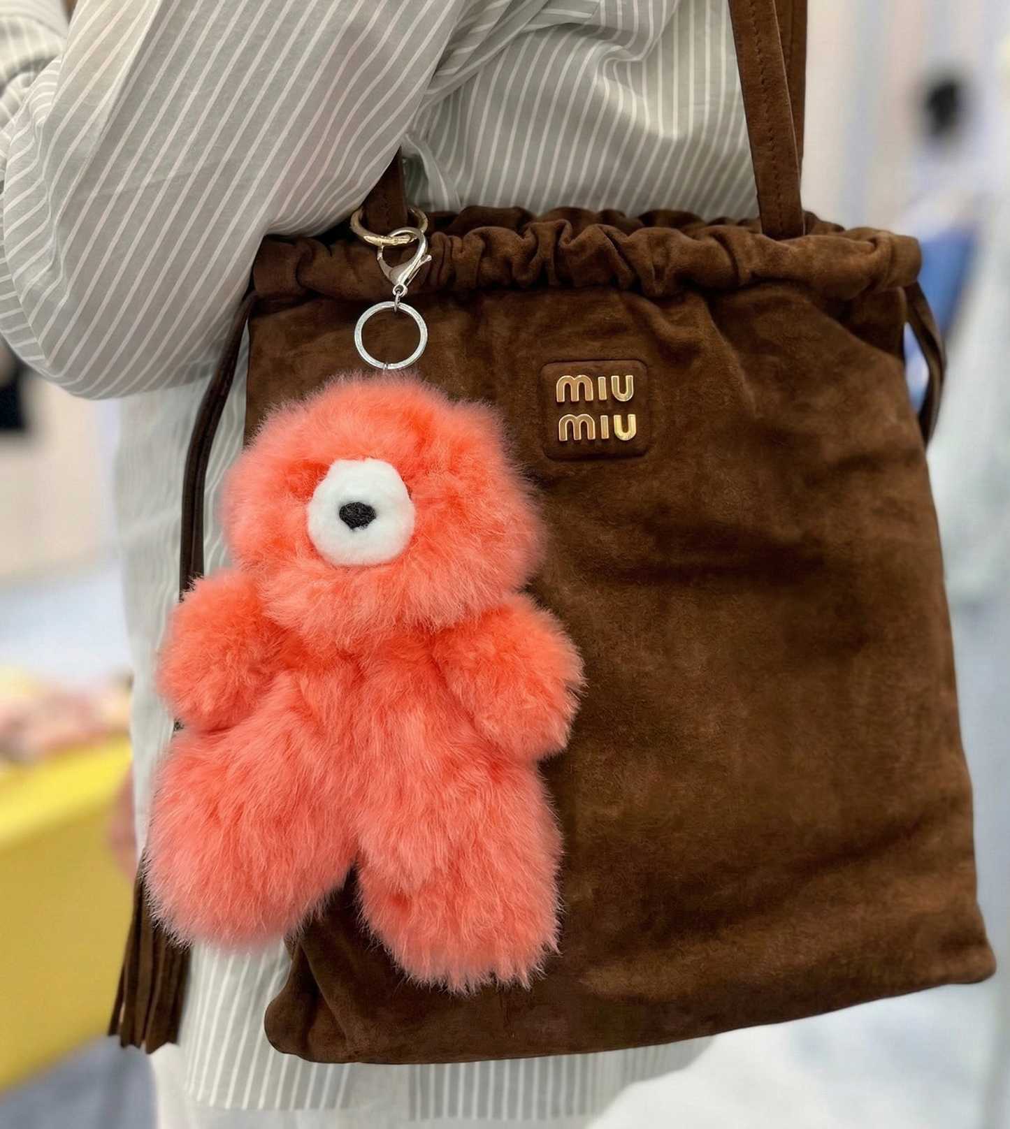 Coral orange alpaca bear keyring hanging from a brown velvet drawstring shoulder bag, street style outfit shot with striped shirt
