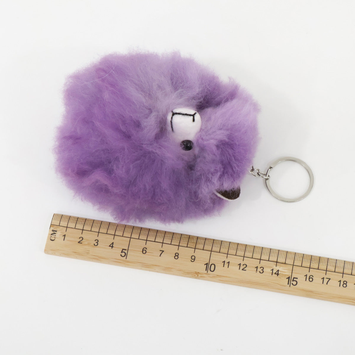 Purple fluffy keychain with a ruler for scale on a white background