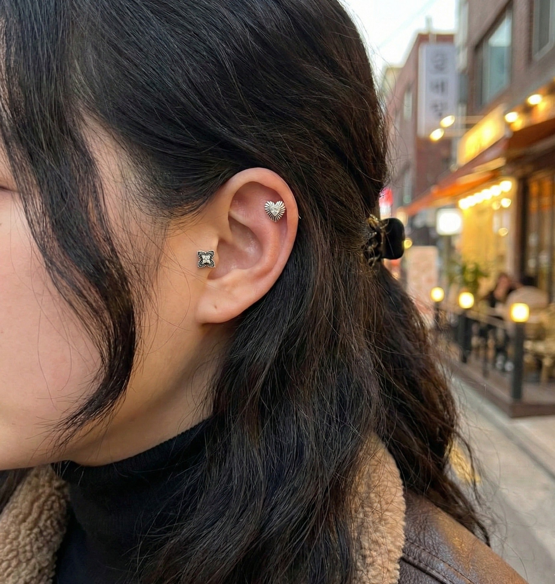 Model wearing antique heart stud on helix and flower stud on lobe with street background