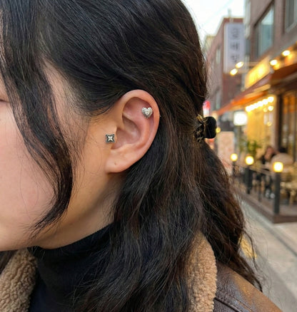 Model wearing antique heart stud on helix and flower stud on lobe with street background