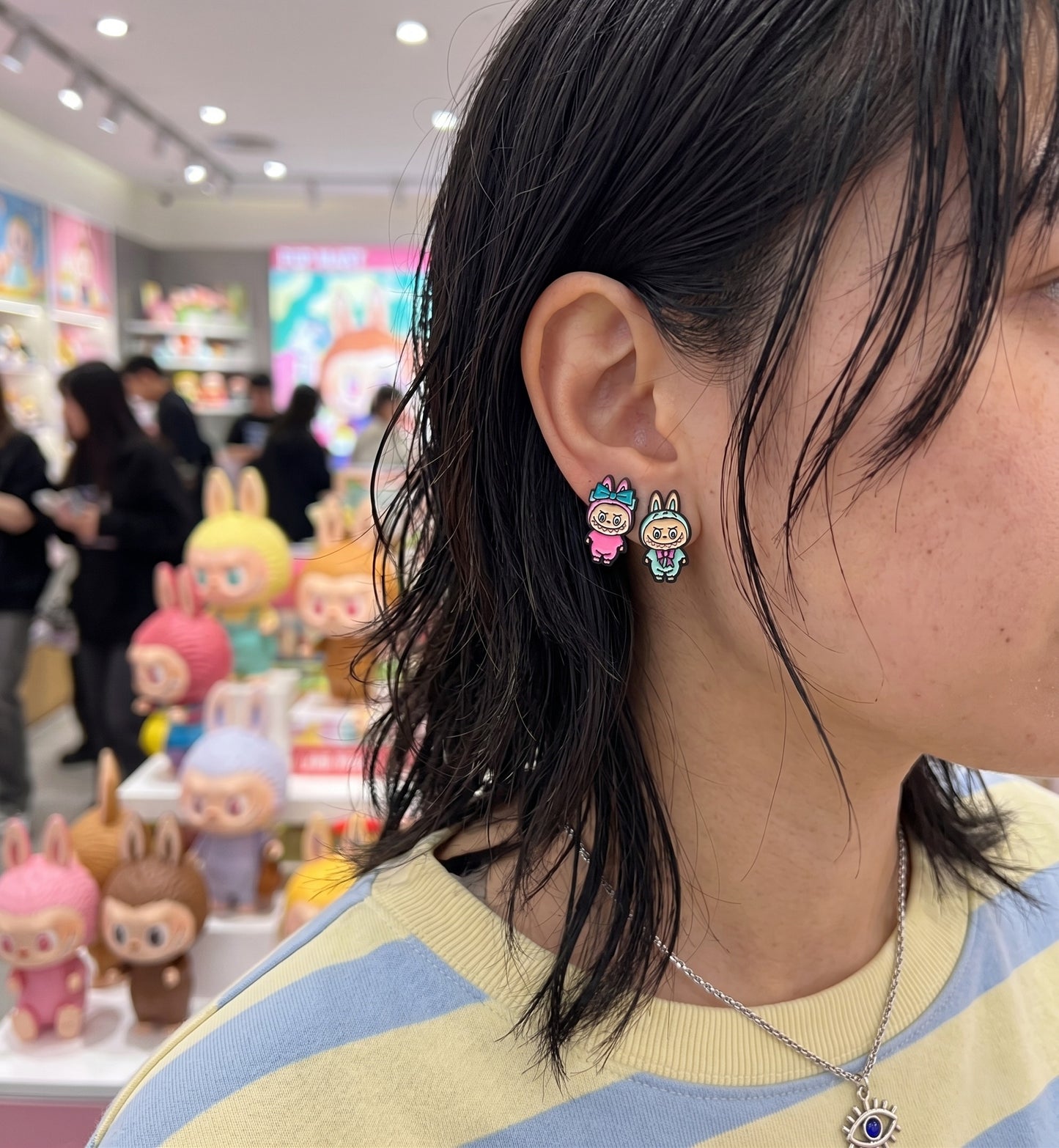 Street style ear stack with Labubu full-body earrings mint and pink mismatch, evil eye layered necklace streetwear aesthetic.