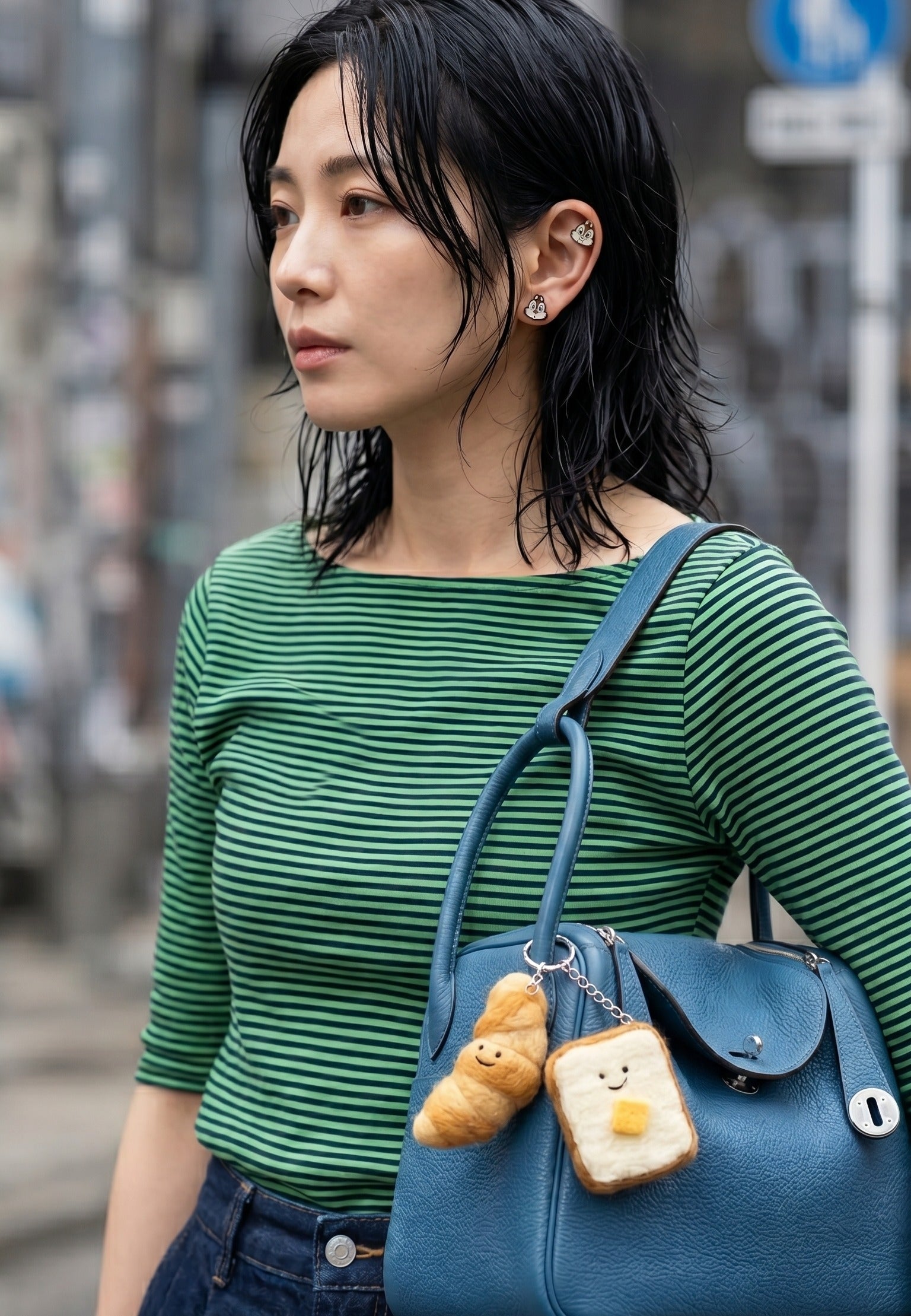 
K-fashion street style full shot — green stripe top, blue leather bag with croissant and toast wool felt bag charms, Chip and Dale piercing ear curation